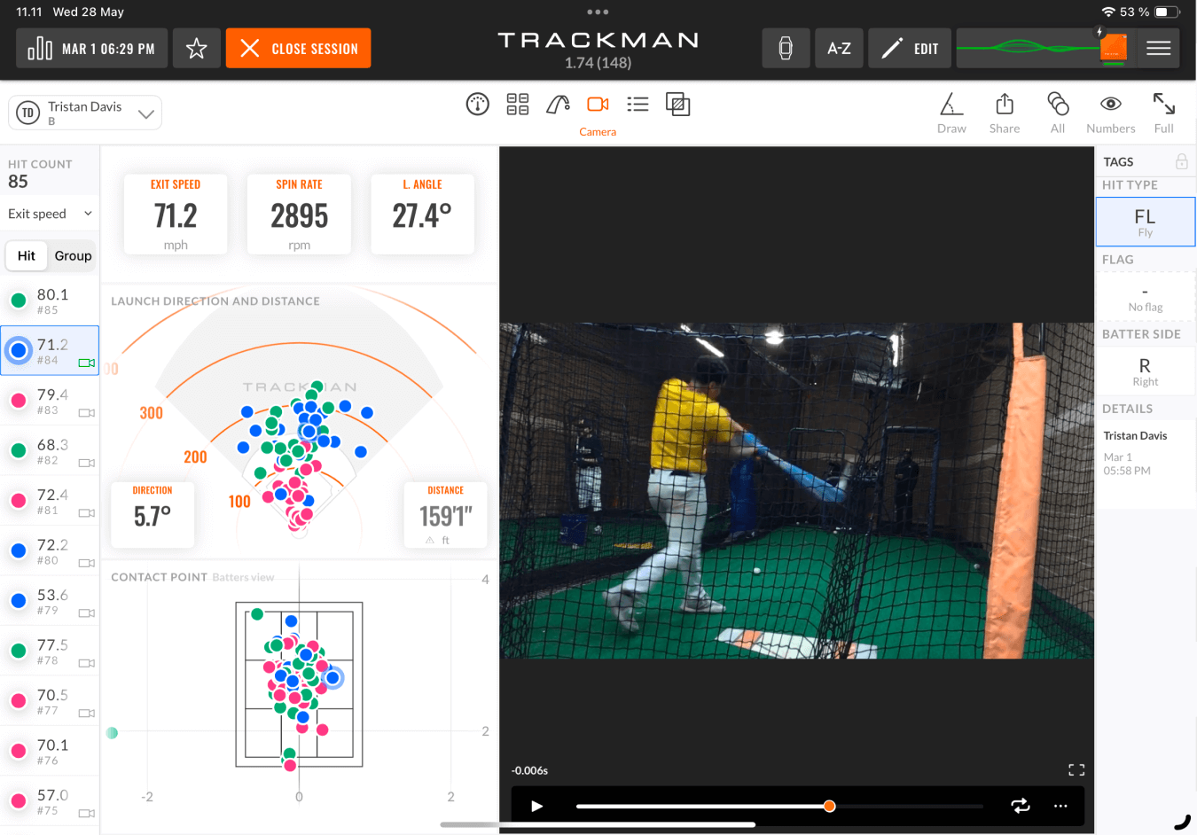 A person swings a baseball bat in an indoor Trackman facility, with data on swing speed and ball trajectory displayed on a screen.