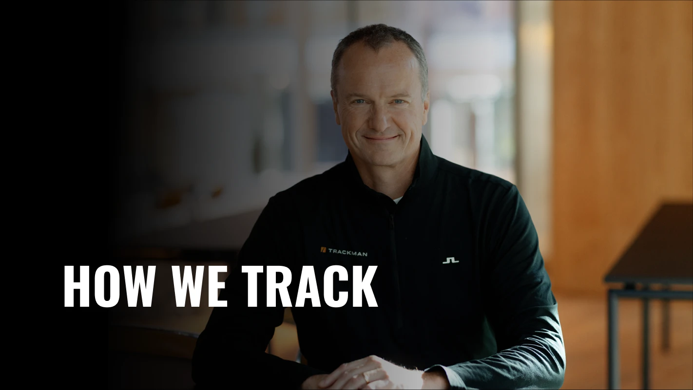 Man in a black jacket smiling, seated indoors with "HOW WE TRACK" text on the left side against a blurred background.