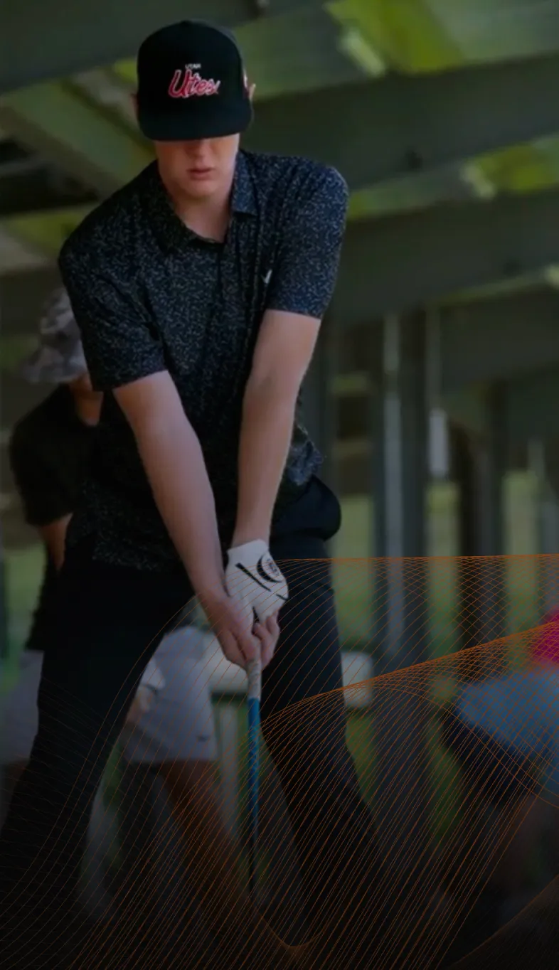 Person in a black cap and shirt holding a golf club, preparing to swing at a driving range.