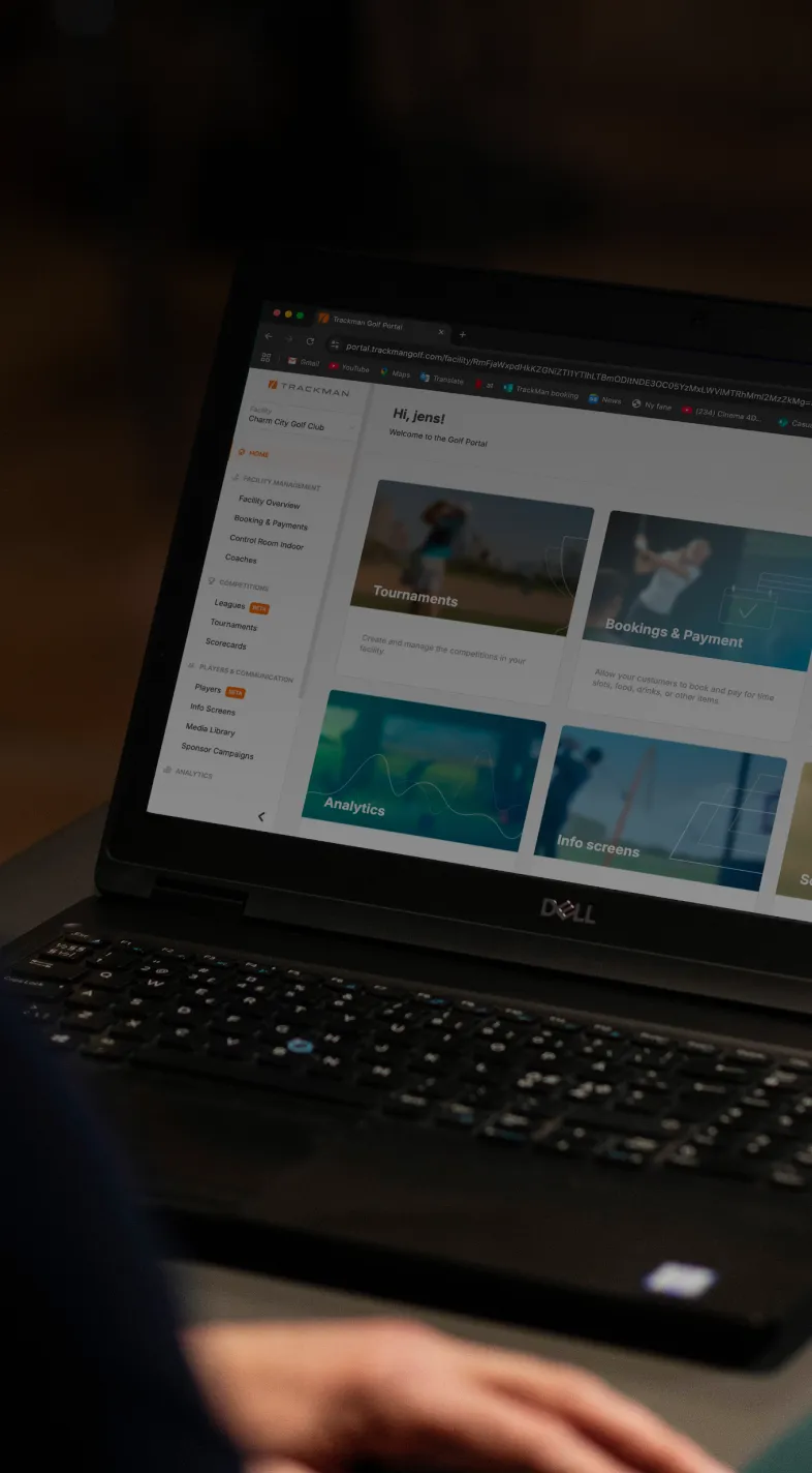 Close-up of a person using a Dell laptop displaying a dashboard with categories like Tournaments, Bookings & Payment, and Analytics.