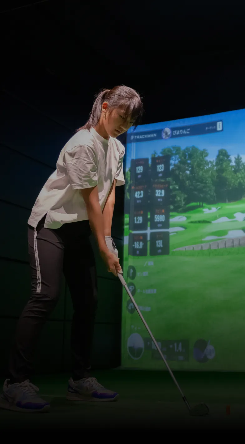 Person playing indoor golf with a simulator, holding a club and preparing to swing. Screen shows golf course and data.